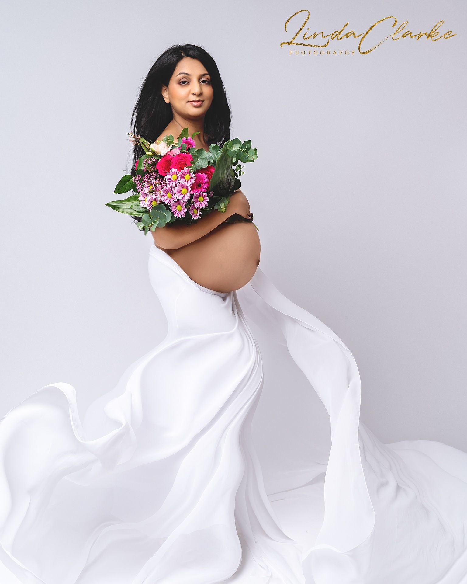 Pregnant lady holding a bouquet of flowers and wearing a white dress
