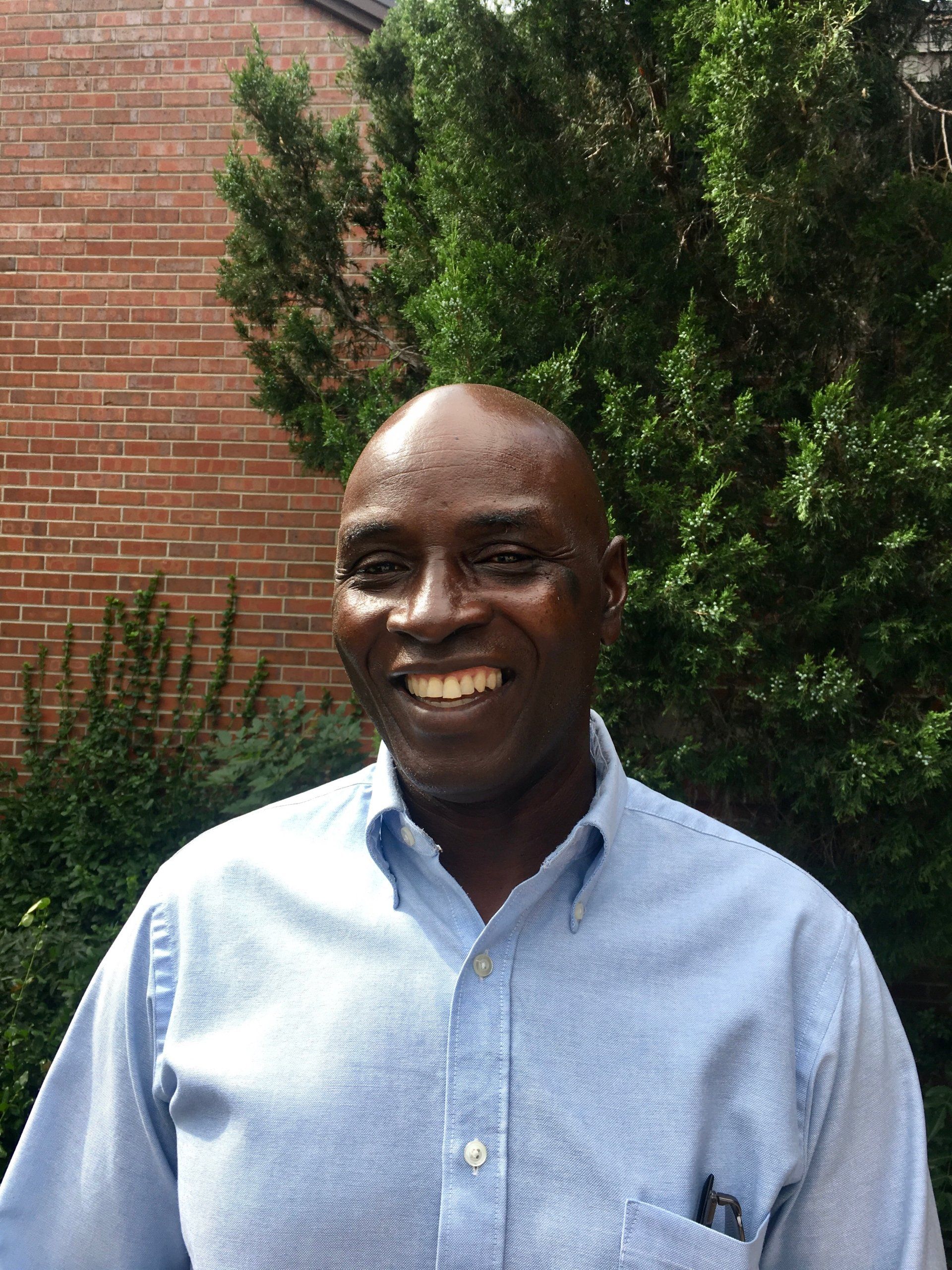 A cheerful photo of Patrick Lutalo wearing a blue shirt, displaying a warm smile.