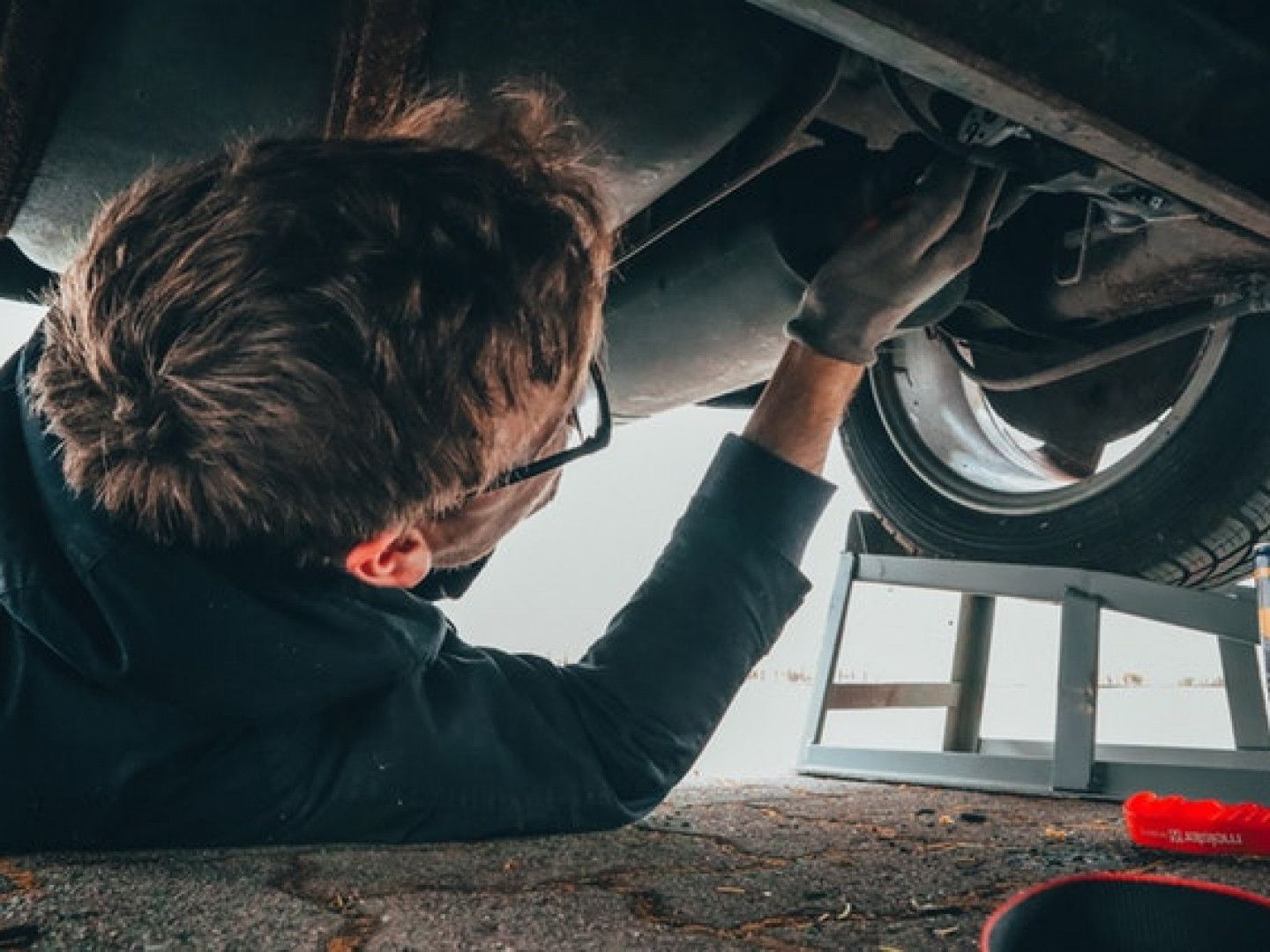 Mechanic working under a car, inspecting the wheel and undercarriage in a garage.