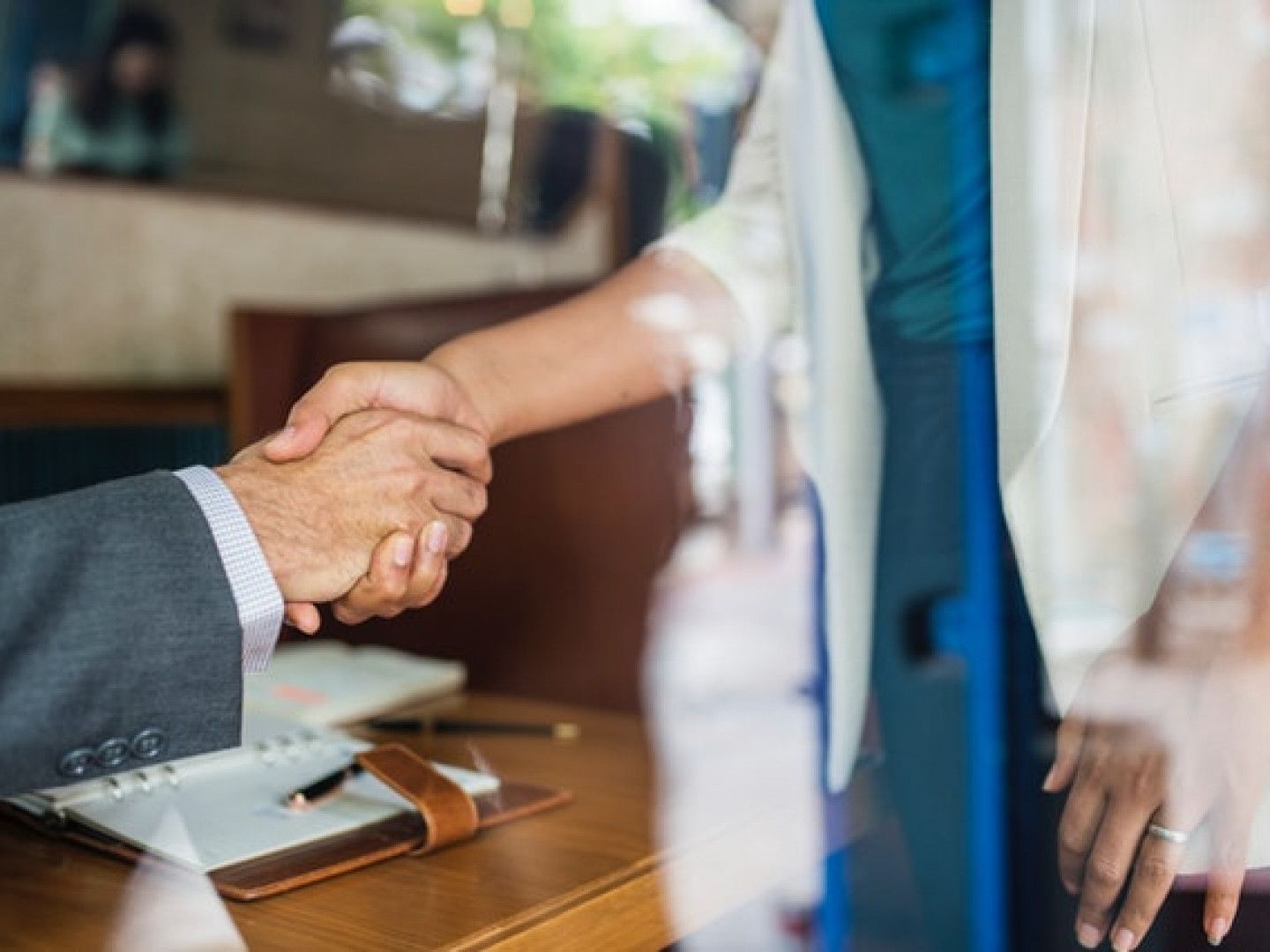 Handshake over a desk with a notebook and pen, suggesting a business agreement