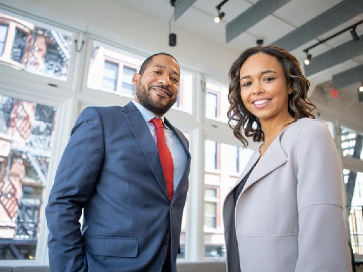 Two business professionals smiling in a modern office with large windows