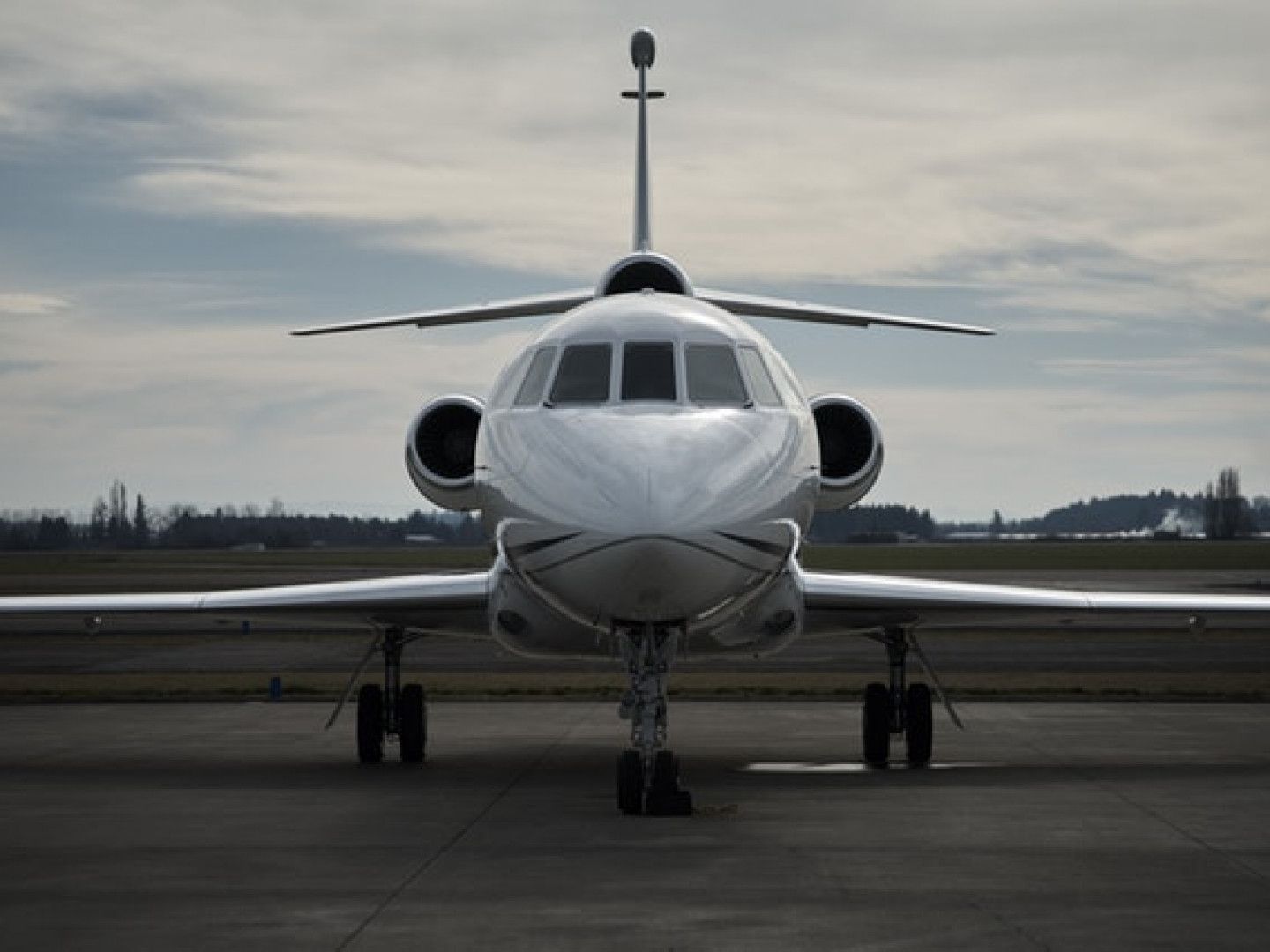 Front view of a small white private jet on an airport runway under overcast skies