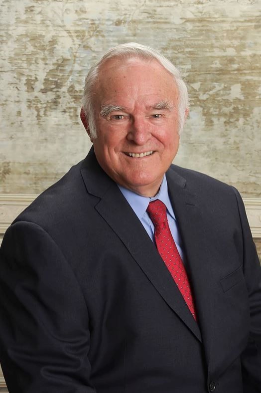 Smiling man in a dark suit and red tie against a neutral textured background
