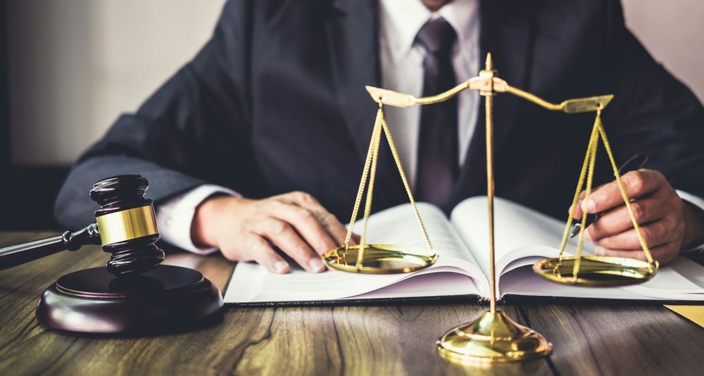 A Judge Is Sitting At A Table With A Book And Scales Of Justice — SJP Law In Maroochydore, QLD