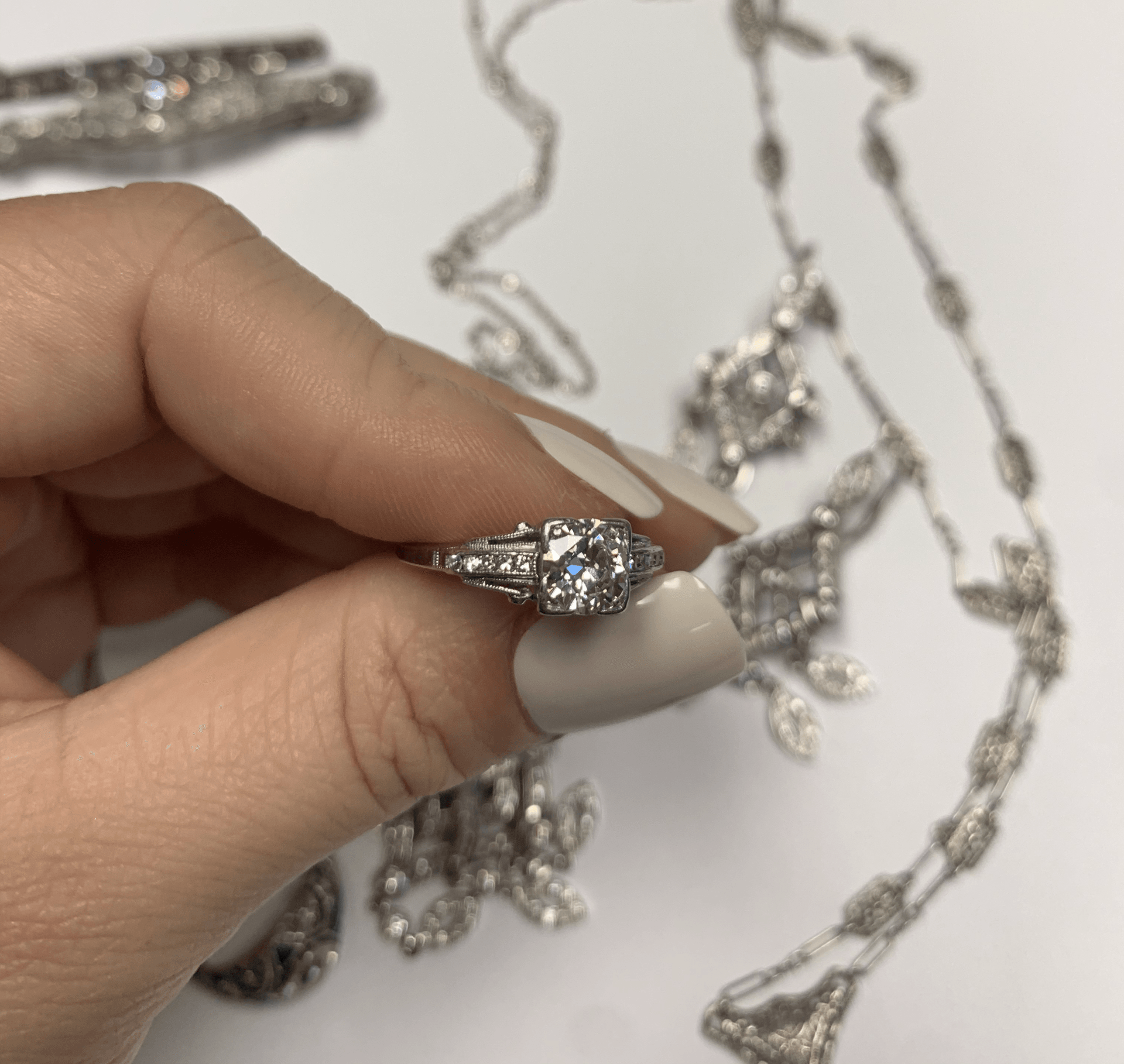 Hand holding a silver ring with a clear gemstone, with matching jewelry on a light background