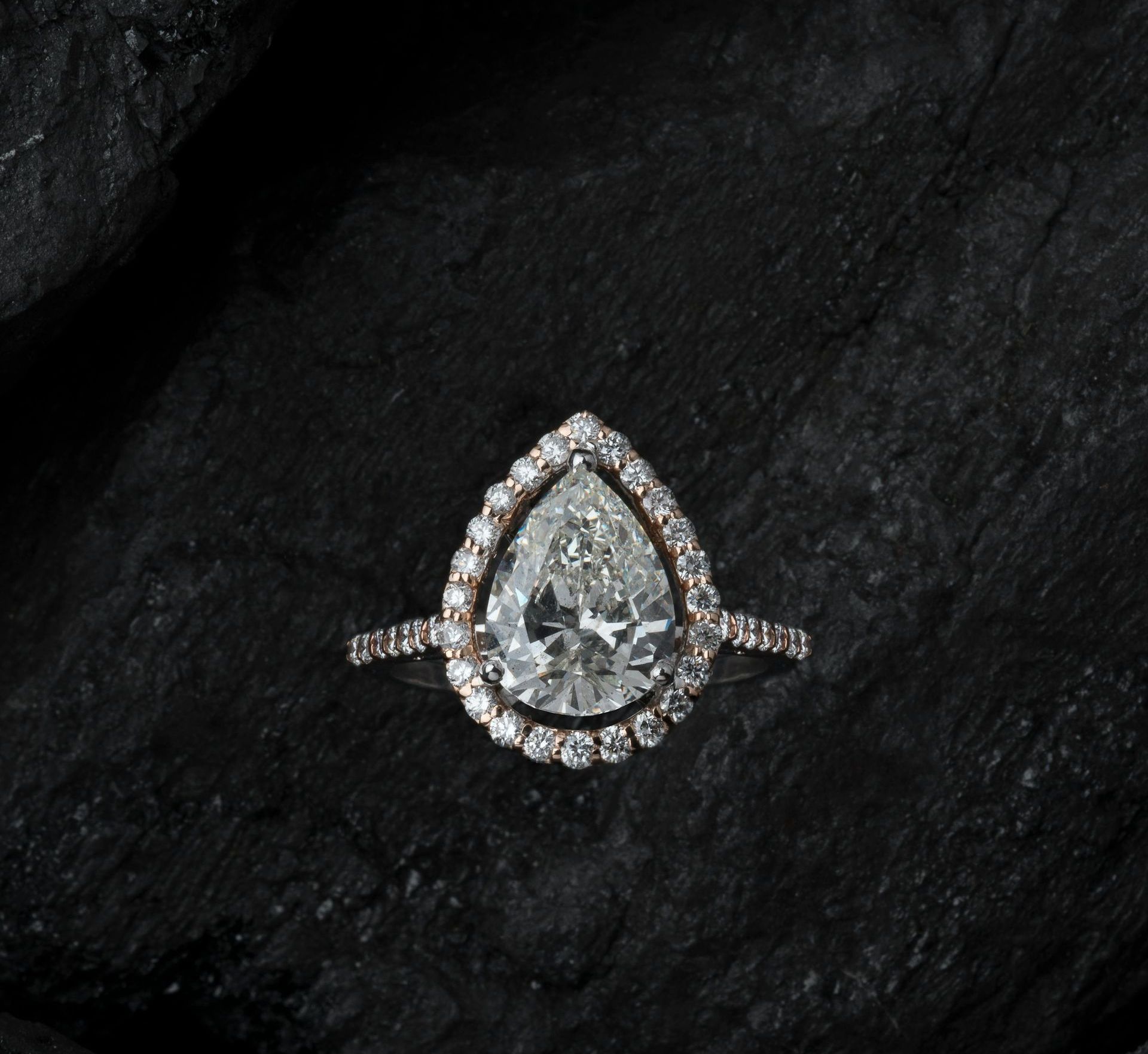 Pear-shaped diamond ring with a halo setting on a dark textured surface