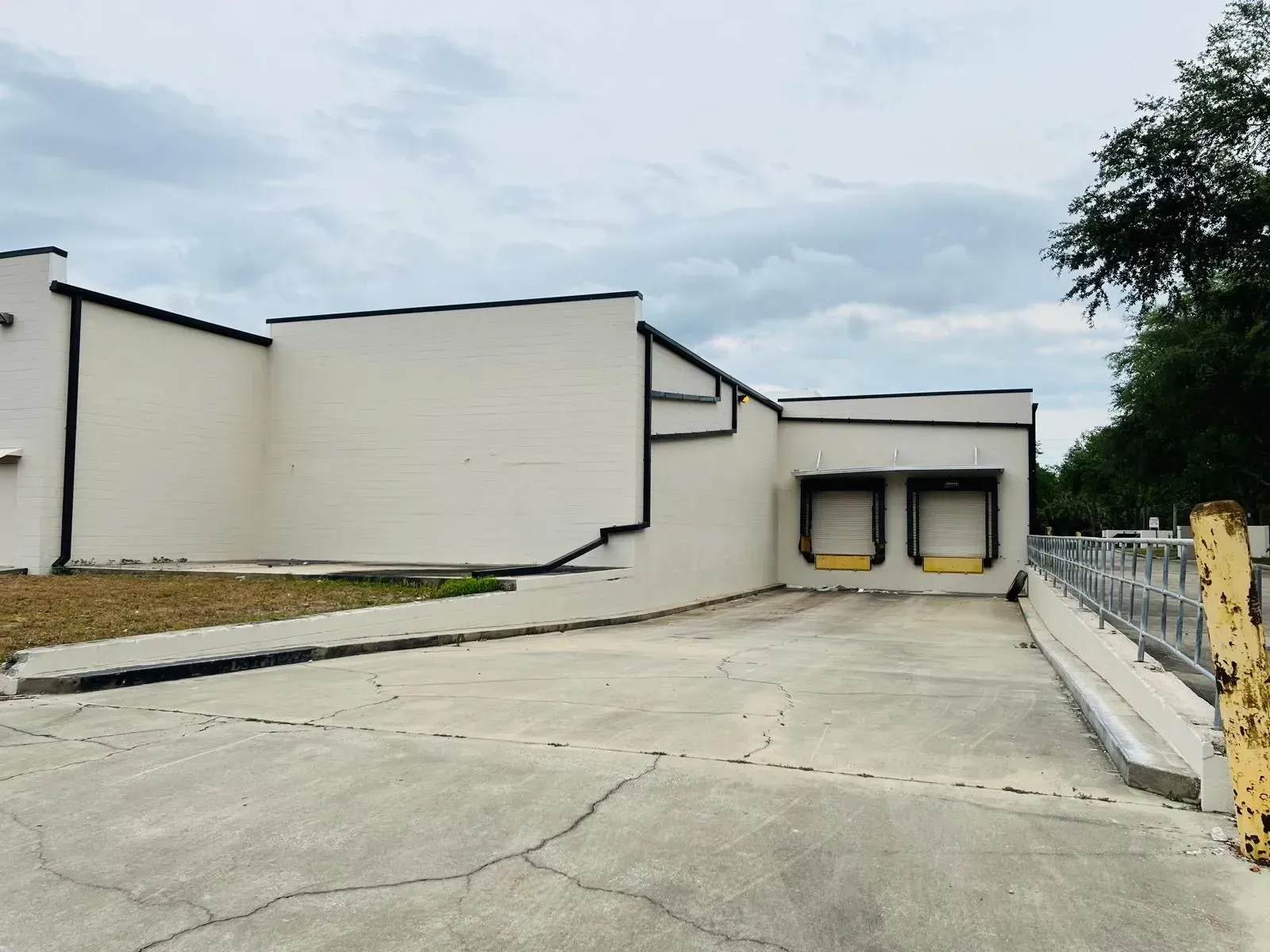 Empty industrial loading dock beside a white building, with a concrete lot and overcast sky