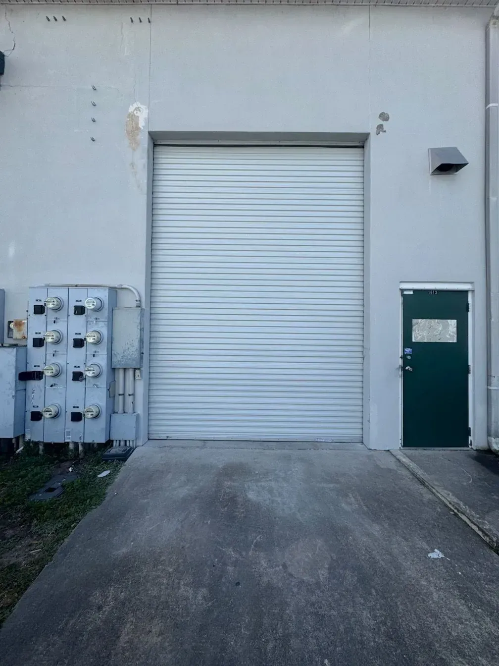 Industrial loading dock with closed white roll-up door, green side door, and electrical panels on a concrete wall