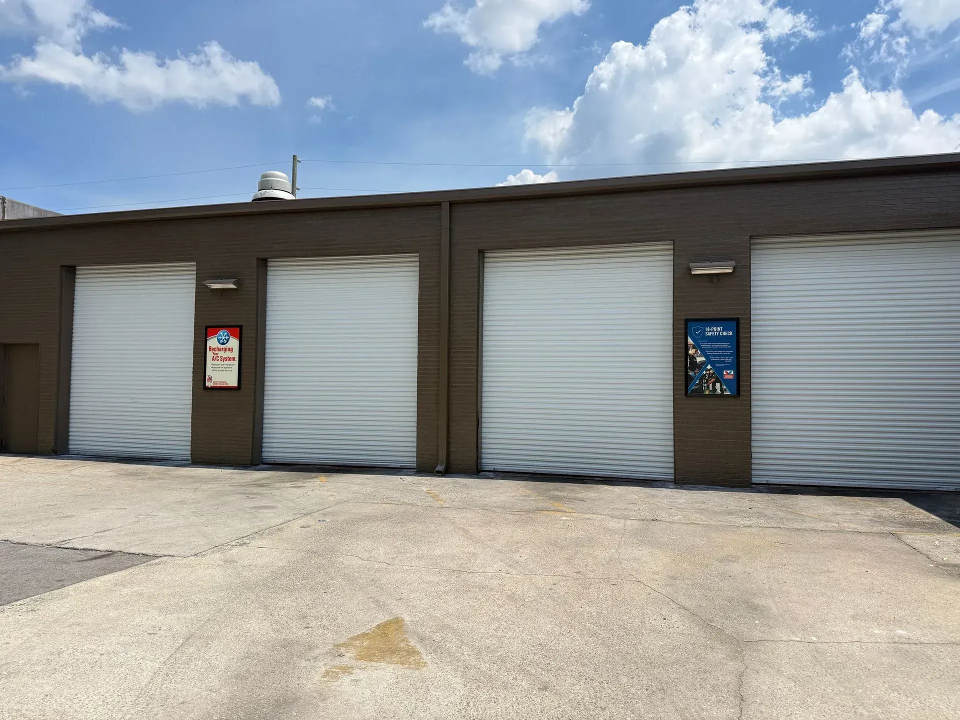 Row of white roll-up garage doors on a brown building under a partly cloudy sky