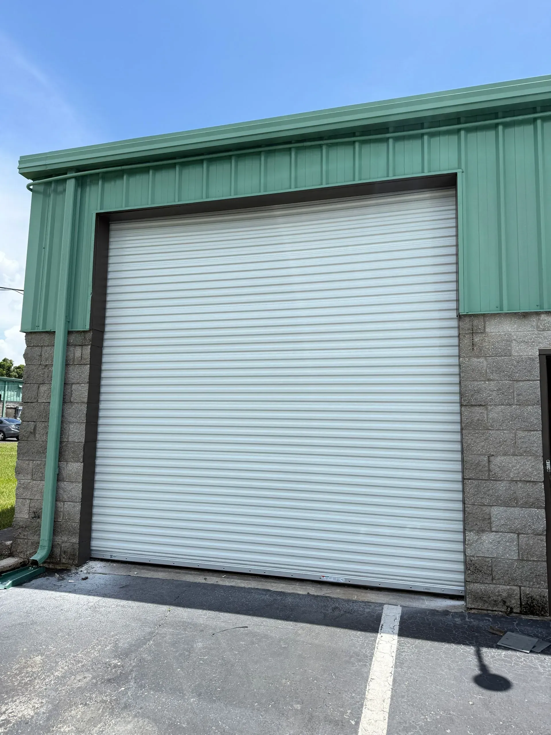 Closed white roll-up garage door on a green metal building