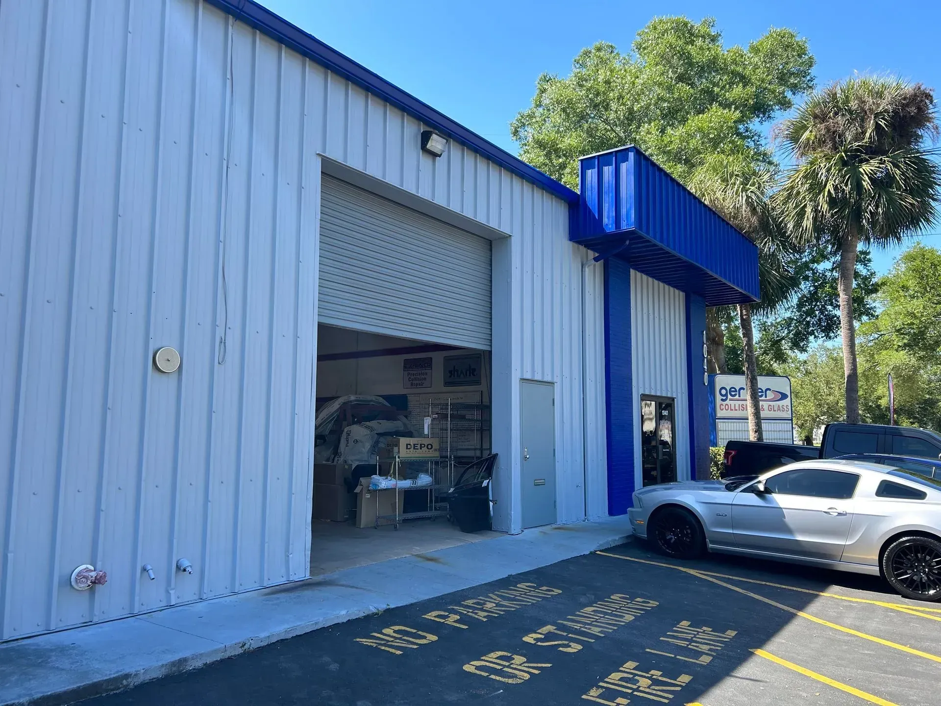 Industrial building with an open garage bay and a white car parked outside in bright sun