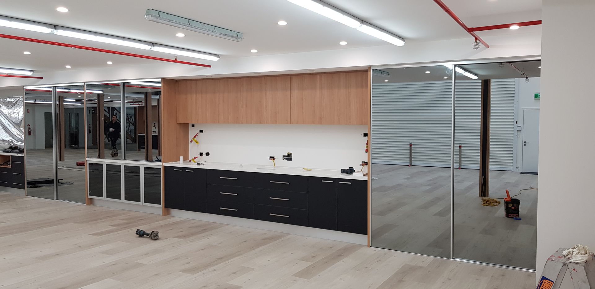A kitchen area under construction in an office space, featuring wood cabinets, black base cabinets, and mirrored panels.