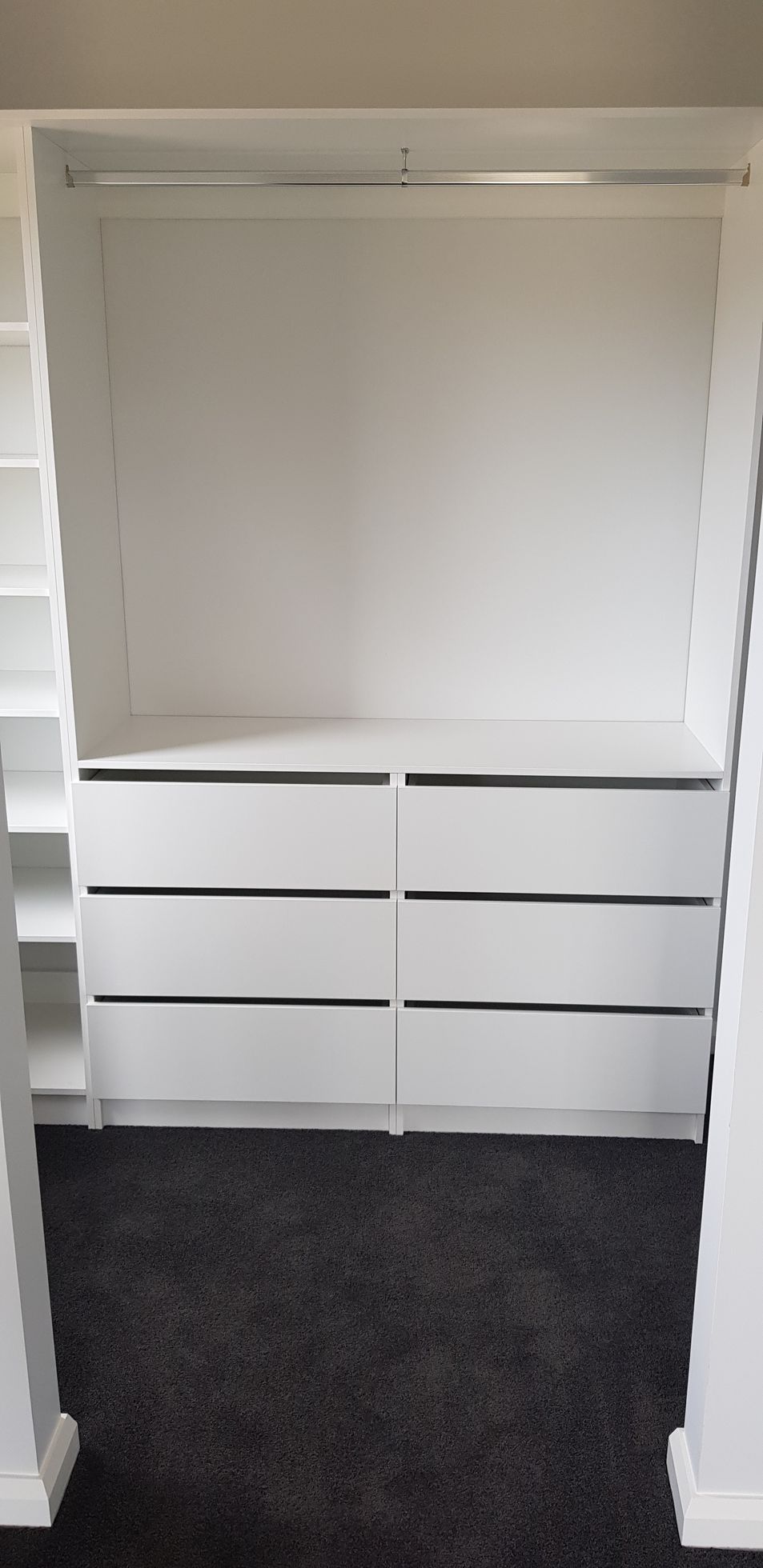 A walk in closet with white drawers and a black carpet.