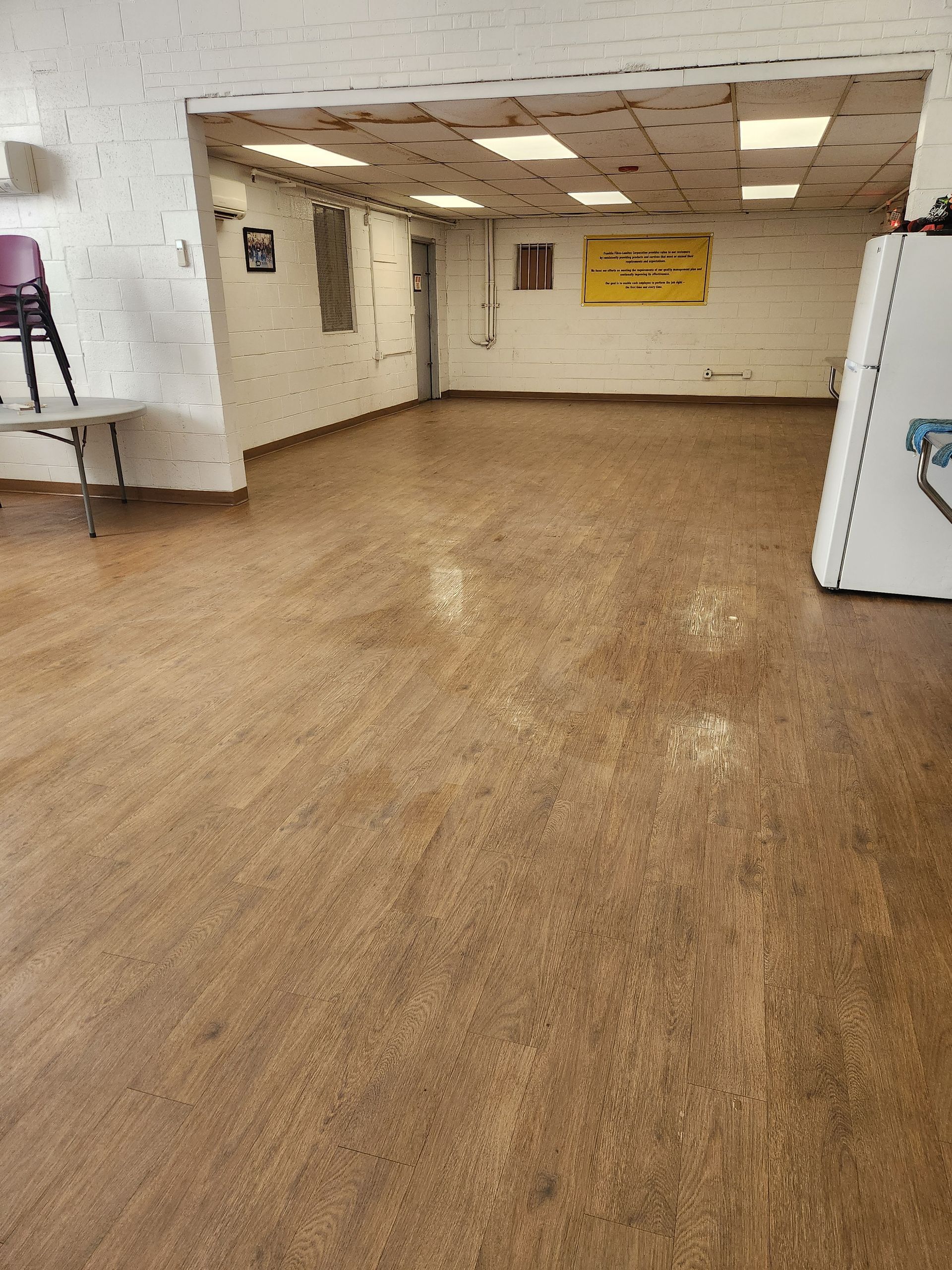 A wide-angle interior view of an empty room with speckled brown flooring, white brick walls, and a recessed ceiling.