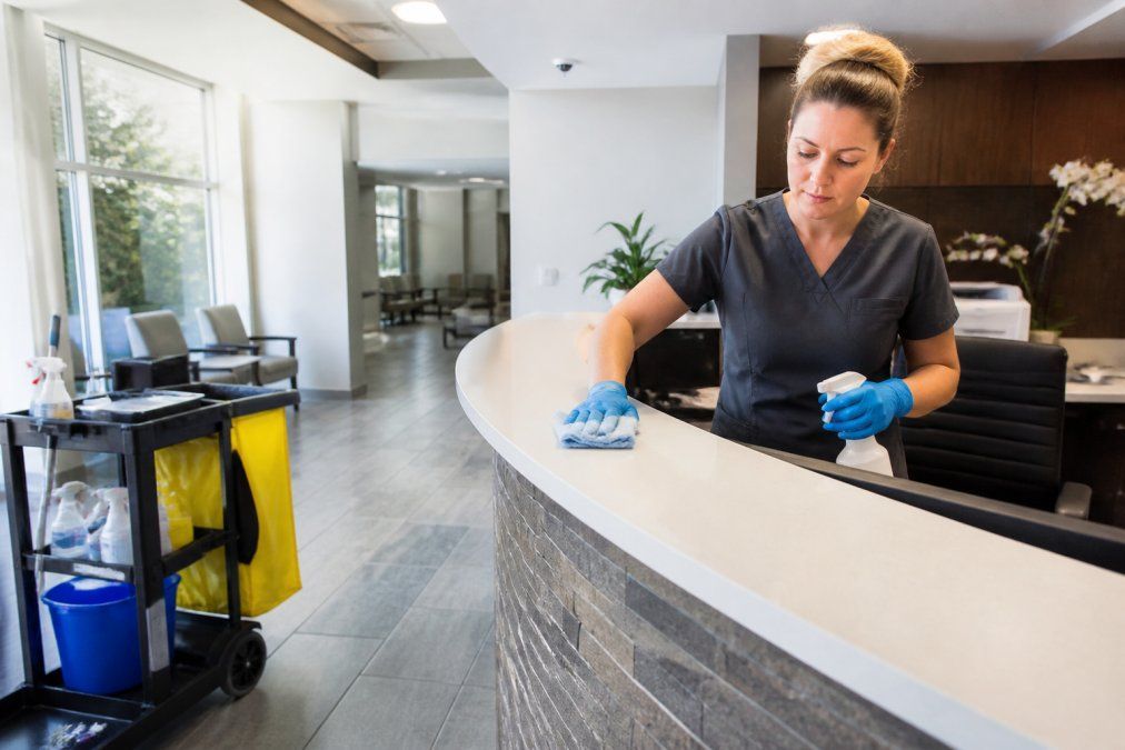 Janitorial staff member cleaning a high-touch surface in a bright, modern medical office reception area