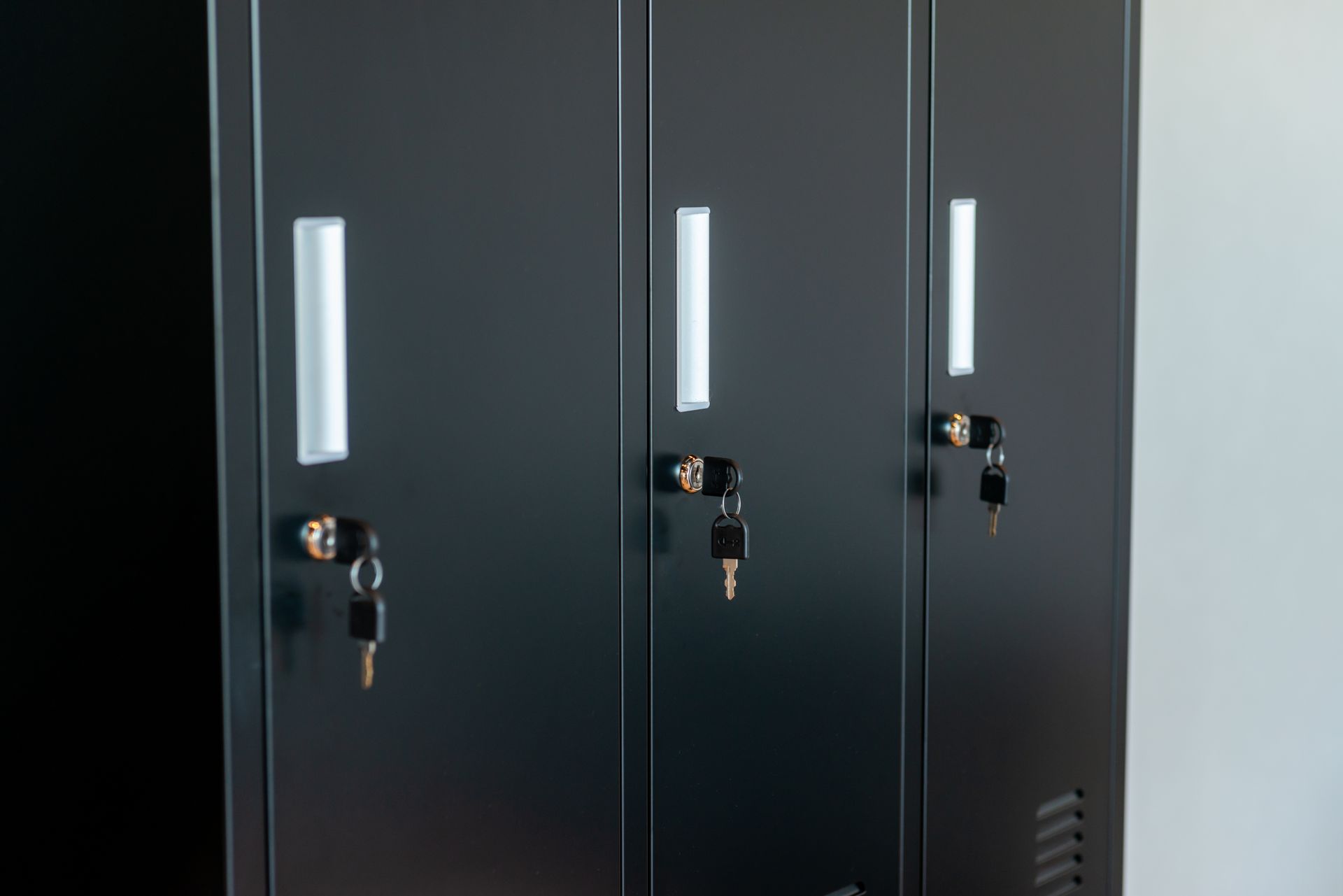 Three black metal lockers with silver handles, each with a key in the lock.