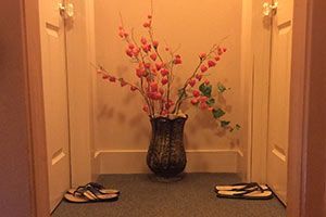 A vase of flowers is sitting on the floor next to a pair of flip flops.