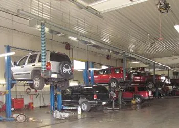 Vehicles raised on lifts inside an auto repair shop. Several SUVs and trucks are in various states of repair.