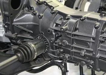 Dark gray car transmission with a half shaft attached.