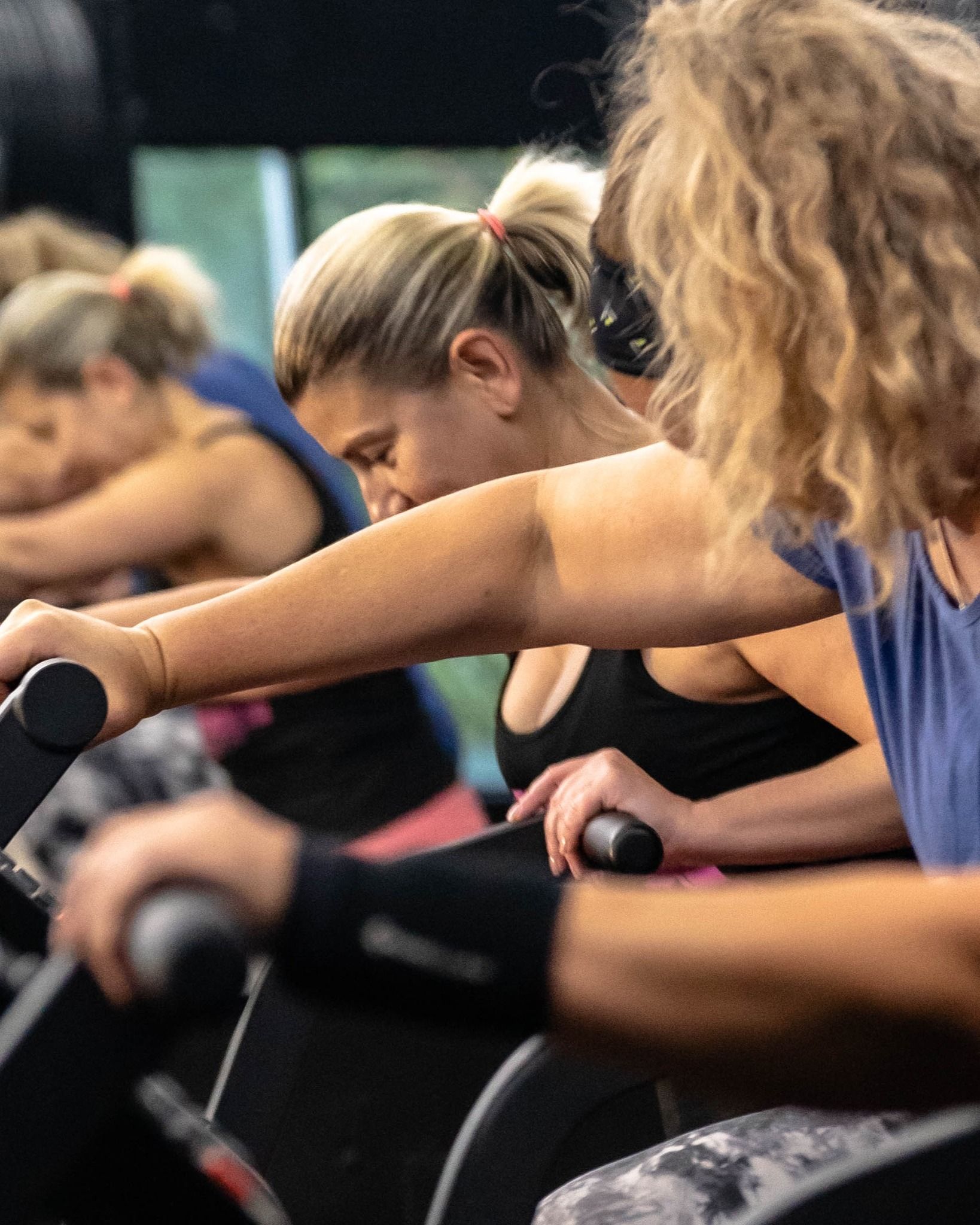 People on exercise bikes leaning forward during a spin class, focused in Revolution Fitness in East Northport, NY.