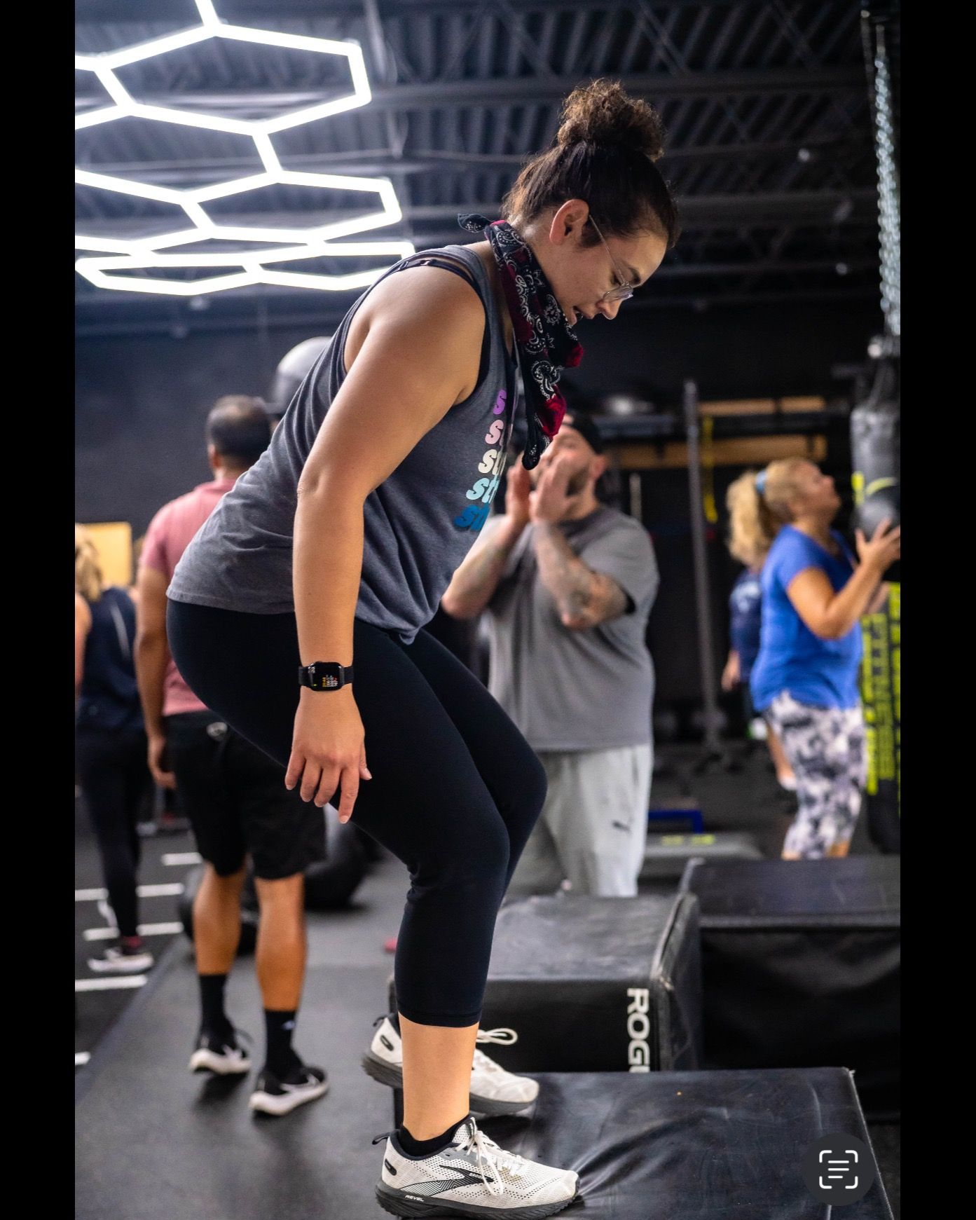 Woman balancing on one foot in a fitness class, with others and neon ceiling lights in the background at Revolution Fitness in East Northport, NY
