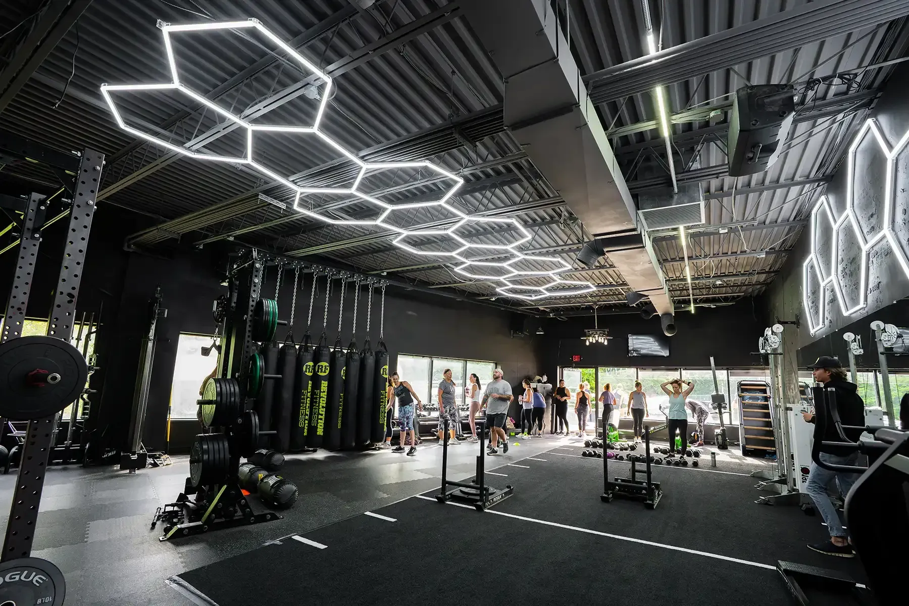 Revolution Fitness in East Northport, NY. Modern gym interior with hexagonal ceiling lights, weight machines, and people exercising