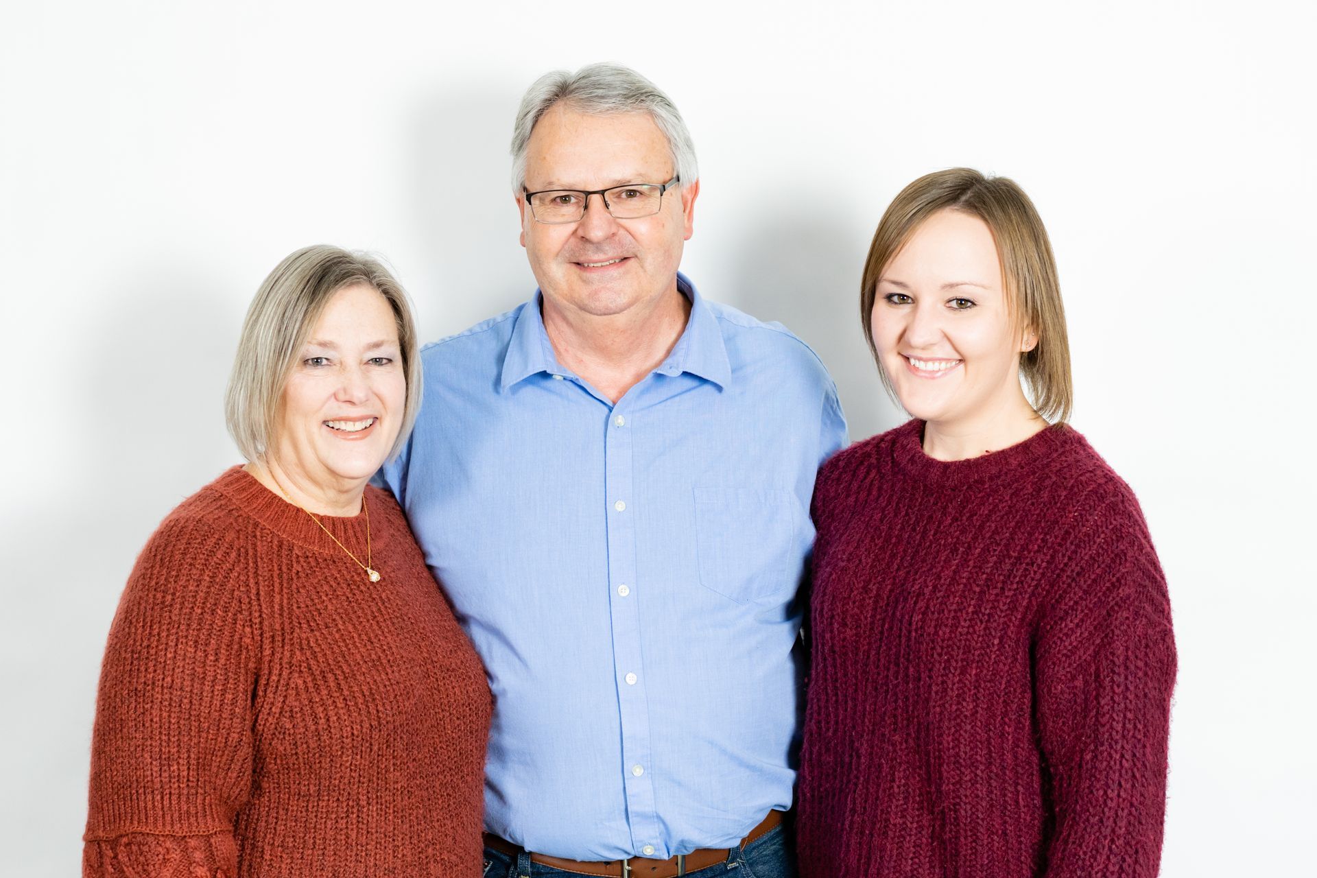 Three smiling people, two women and one man, stand shoulder to shoulder against a white backdrop.