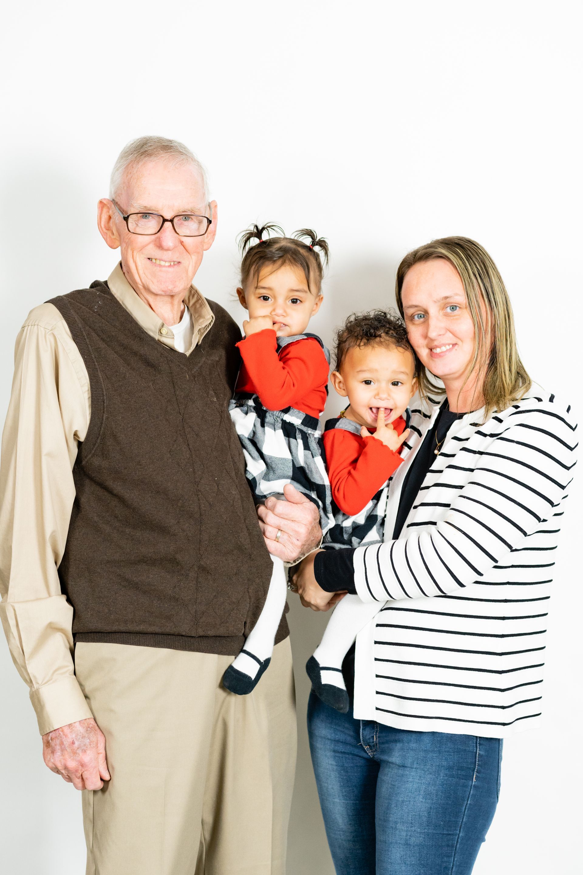 Man, two children, and woman pose for photo against white backdrop. Man holds one child, woman holds the other.
