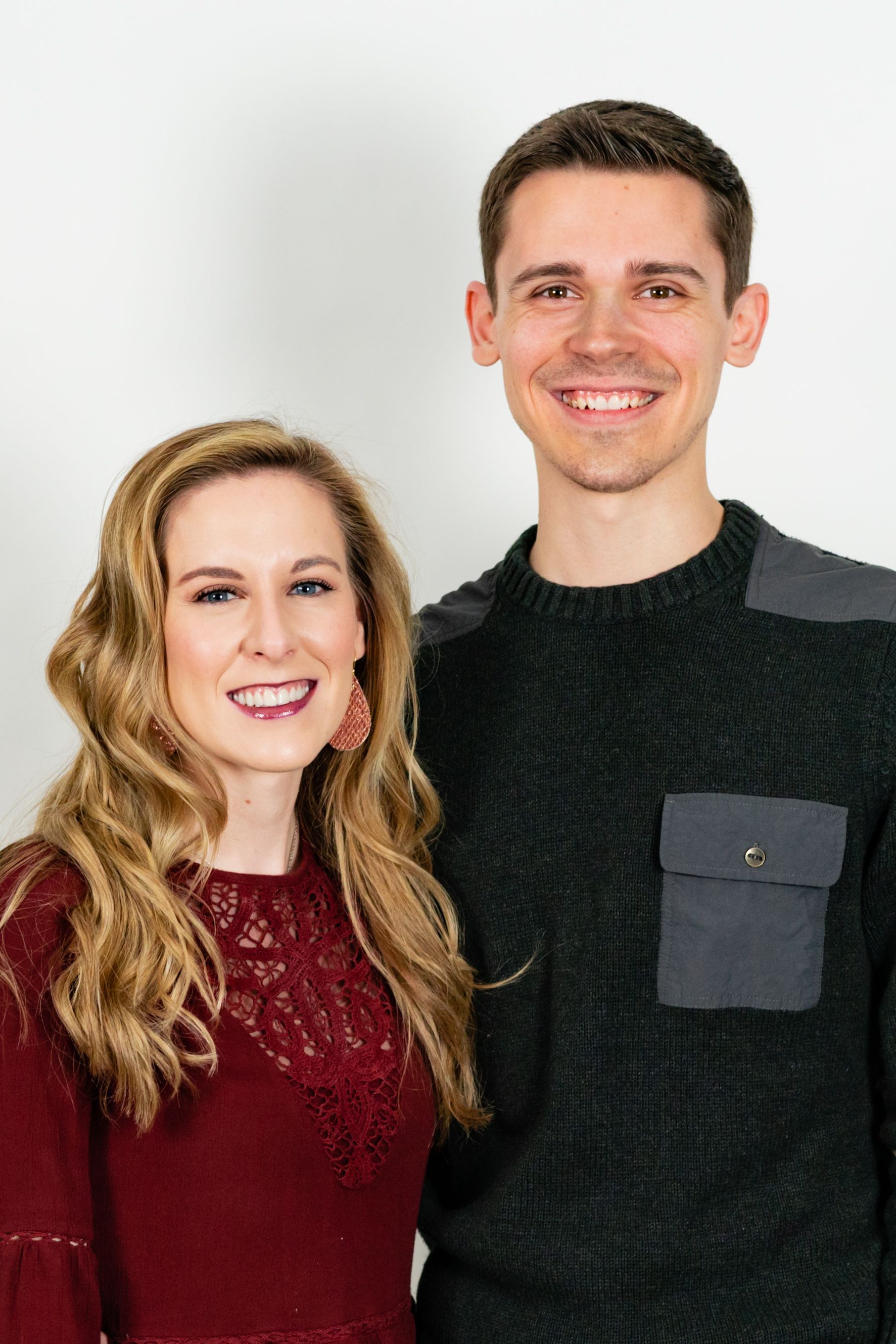 Woman with blonde hair and man smiling, posing in front of a white backdrop.