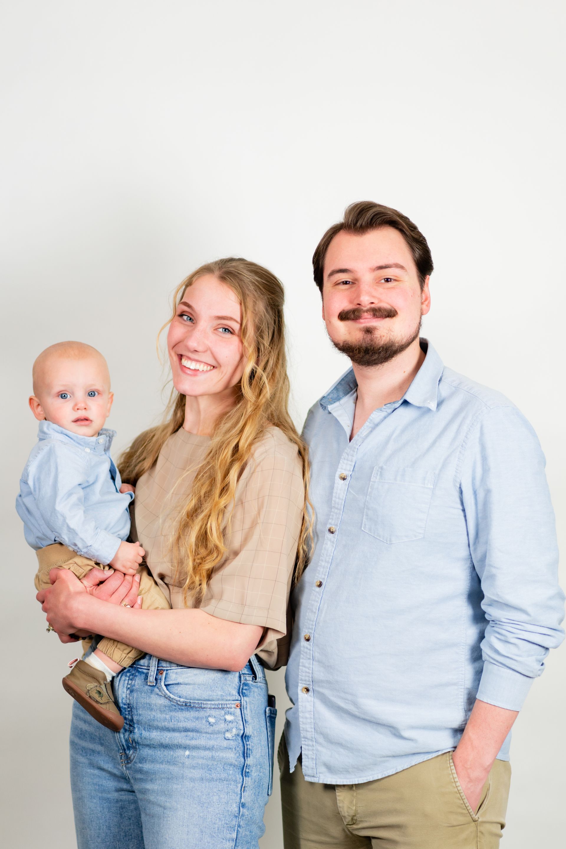 Family of three: mother holding baby, father smiling, all looking at camera.