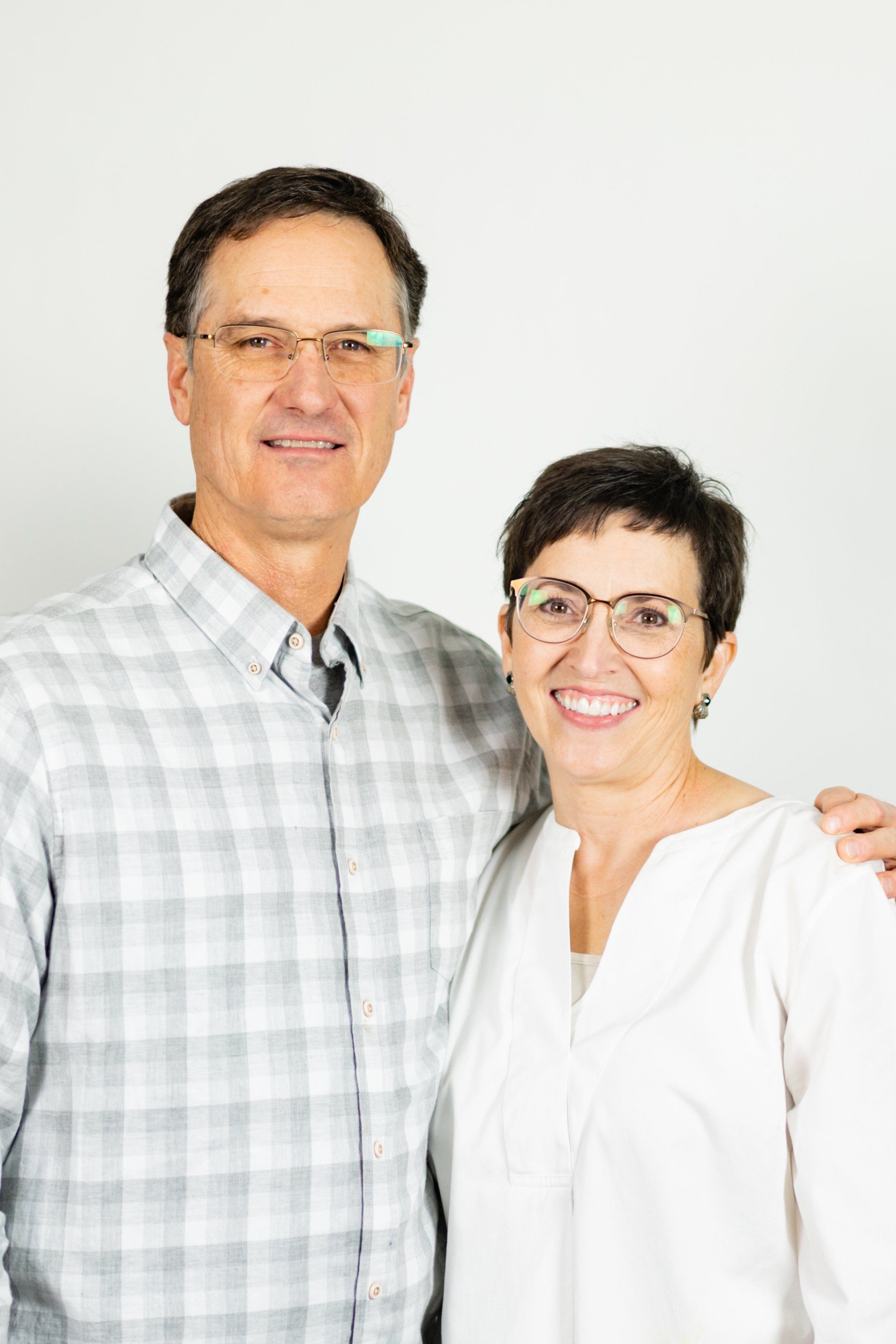 Man and woman, smiling, posing together, wearing glasses, neutral background.