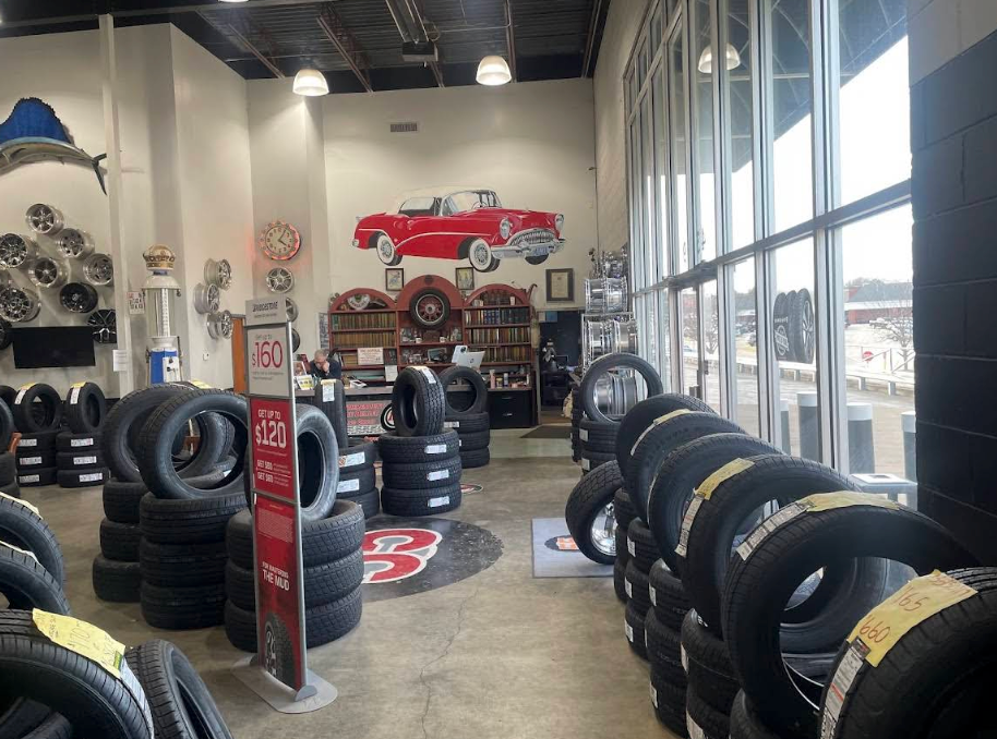 Interior of a tire shop with stacks of black tires on the floor and a wall mural of a vintage red car | 55 Tires and Service