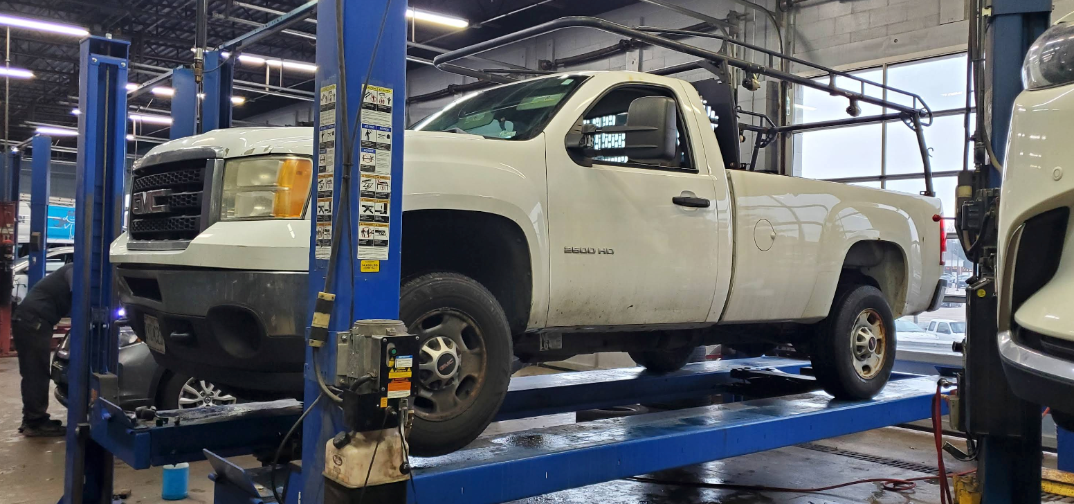A white pickup truck elevated on a hydraulic lift inside an automotive repair shop | 55 Tires and Service