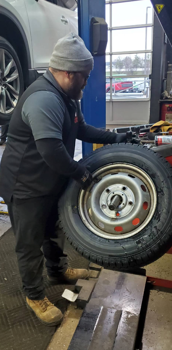 A mechanic in a grey beanie and uniform works on a tire at a shop service bay | 55 Tires and Service