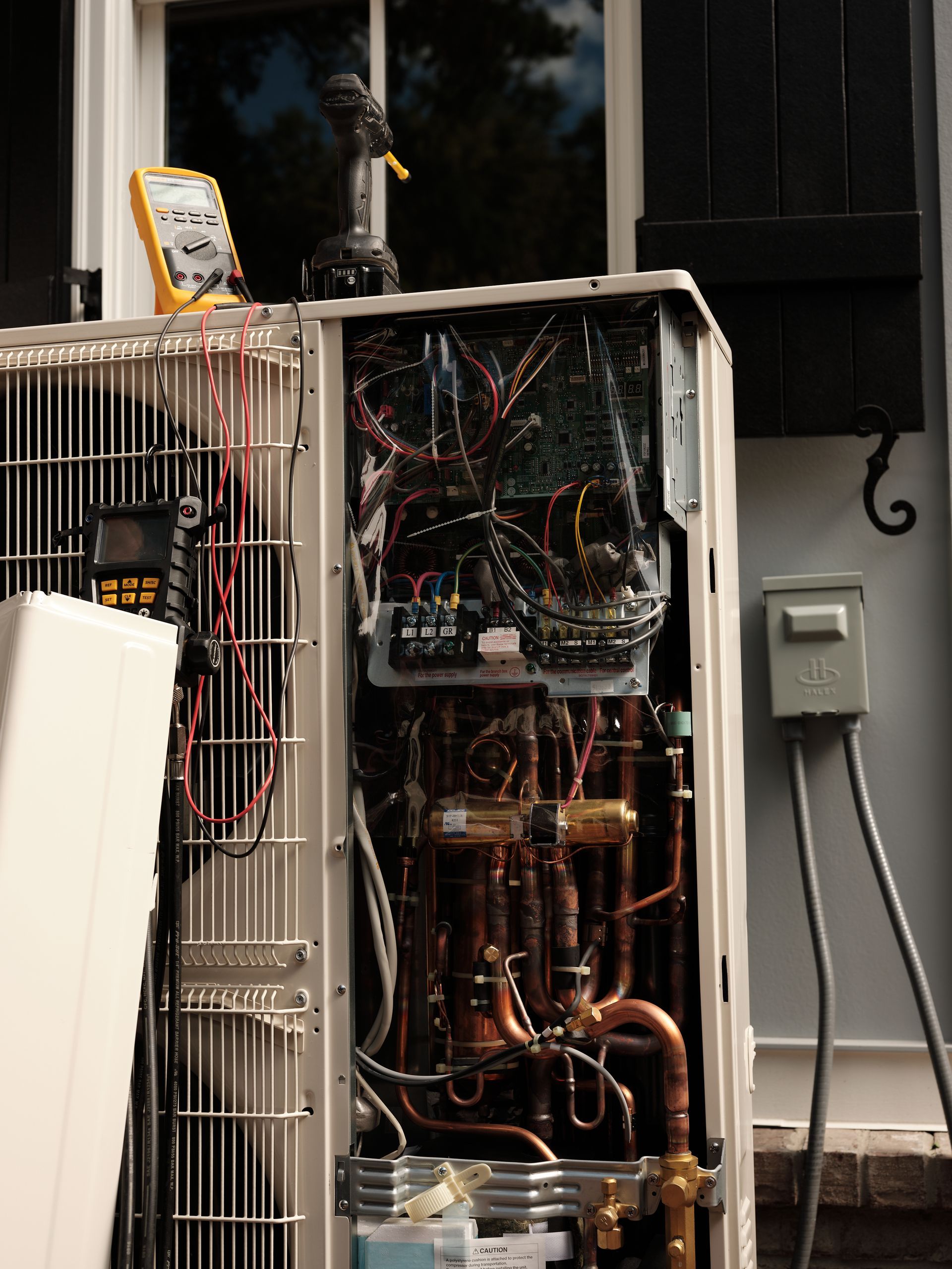 Open air conditioning unit being serviced outdoors, showing wires, copper tubing, and tools.