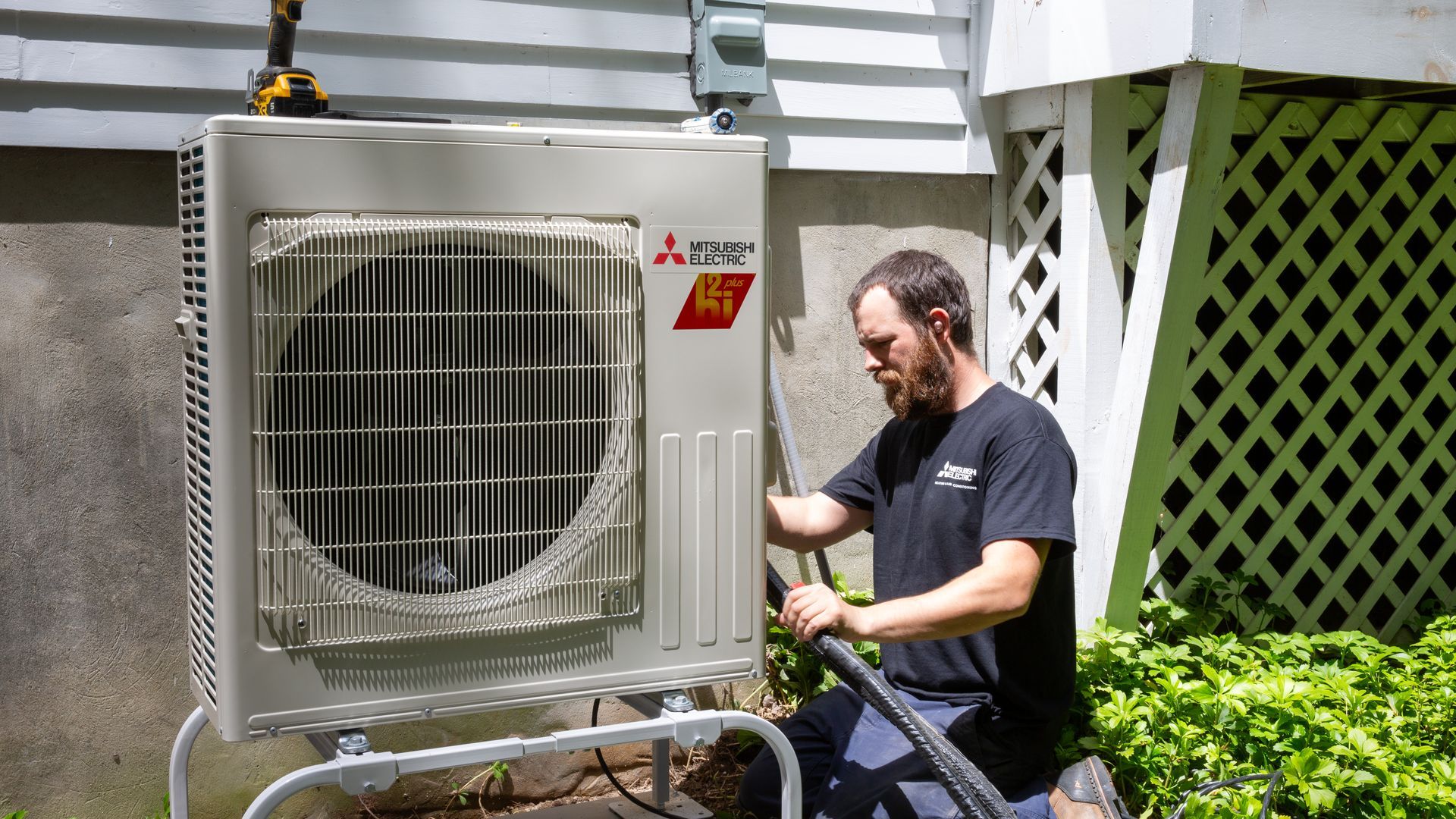 Pfluke Home Services technician servicing a Mitsubishi heat pump unit outdoors.
