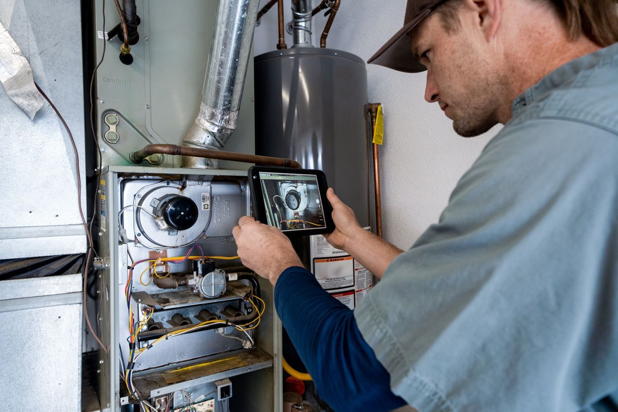Pfluke Home Services technician inspecting a furnace, using a tablet to take a photo.