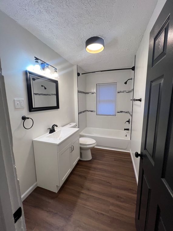 Modern bathroom with white vanity, mirror, toilet, tub, and dark wood floor
