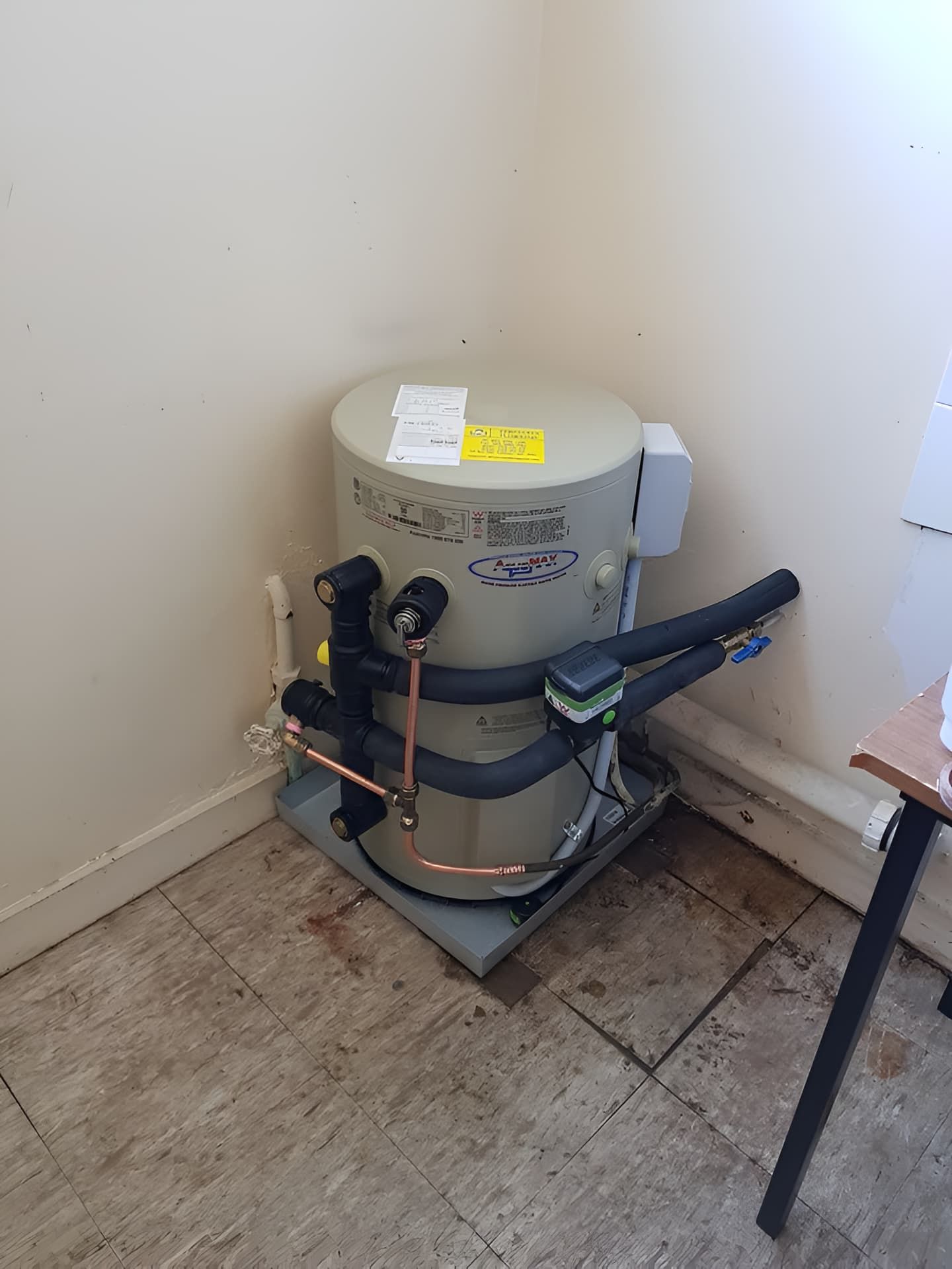 A Water Heater is Sitting in a Corner of a Room Next to a Table — Simpson's Plumbing & Maintenance Service in Dakabin, QLD