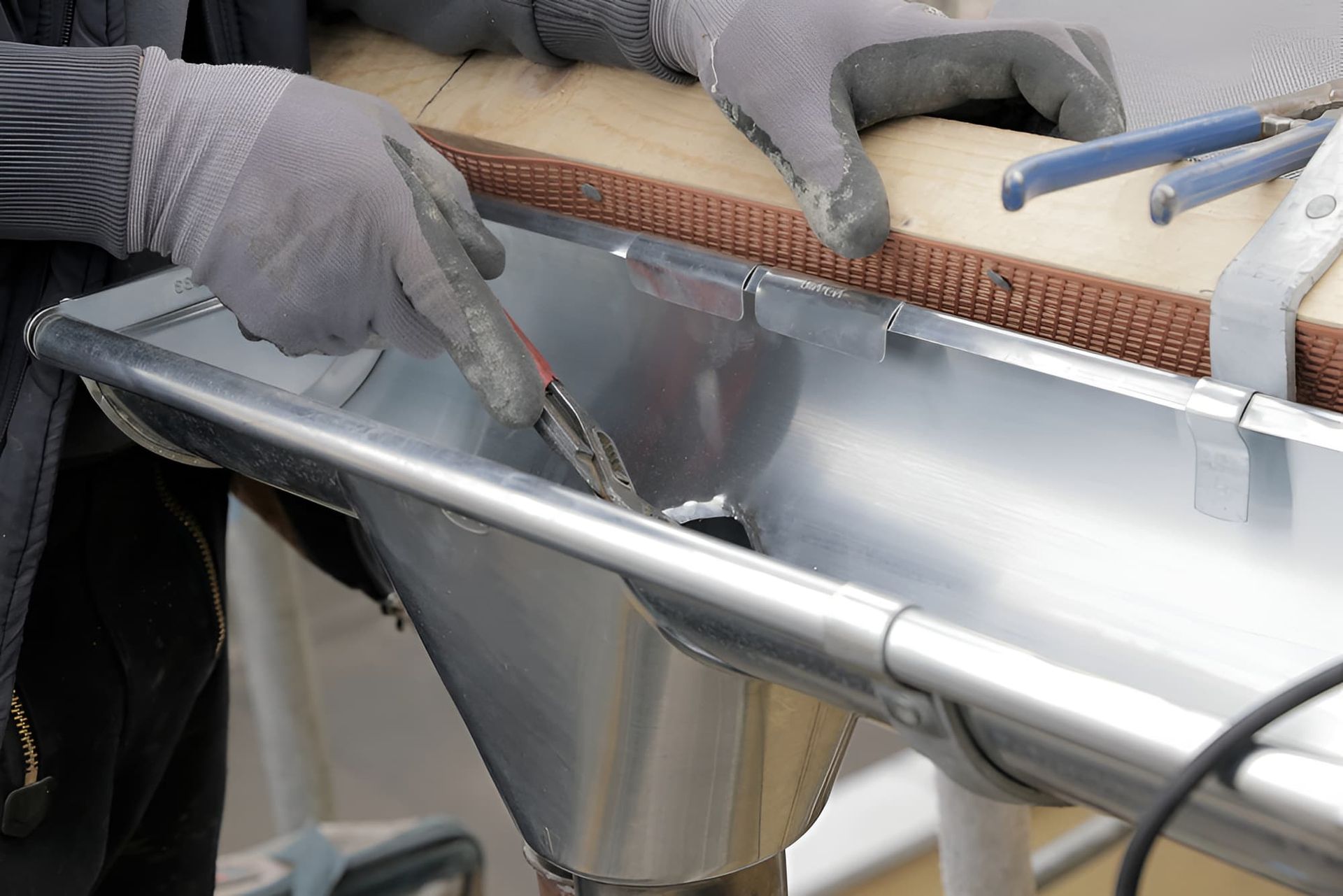 A Man Wearing Gloves is Working on a Metal Gutter — Simpson's Plumbing & Maintenance Service in Dakabin, QLD