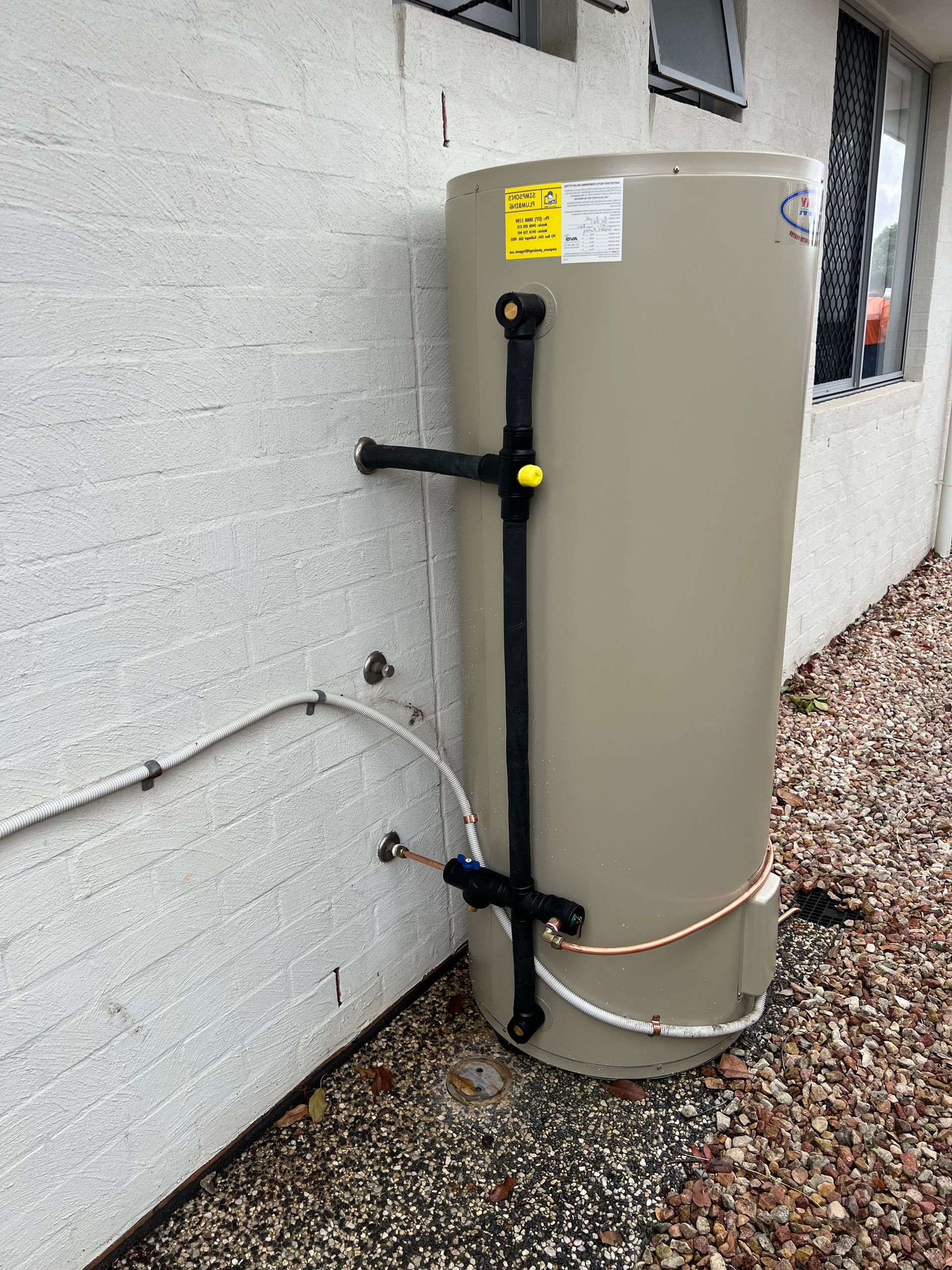 A White Water Heater is Attached to a Brick Wall — Simpson's Plumbing & Maintenance Service in Dakabin, QLD