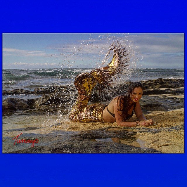 A woman in a mermaid costume is laying on the beach.