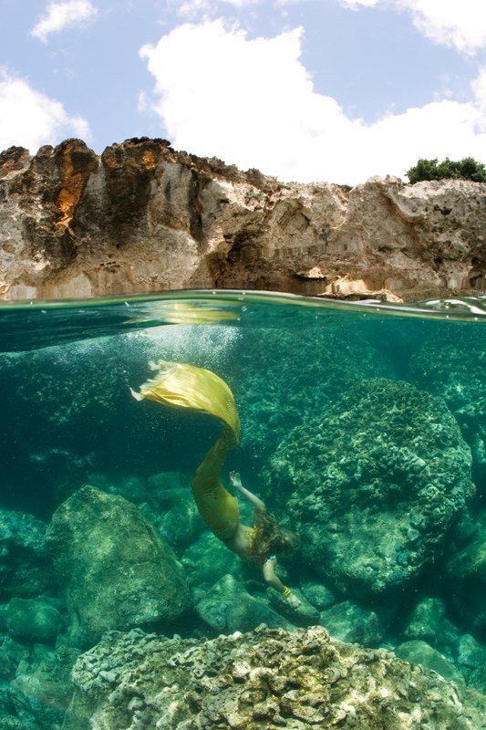A mermaid is swimming in the ocean near rocks