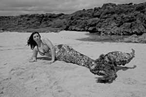 A black and white photo of a mermaid laying on the beach.
