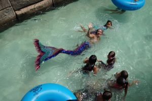 A group of children are swimming in a pool with a mermaid.