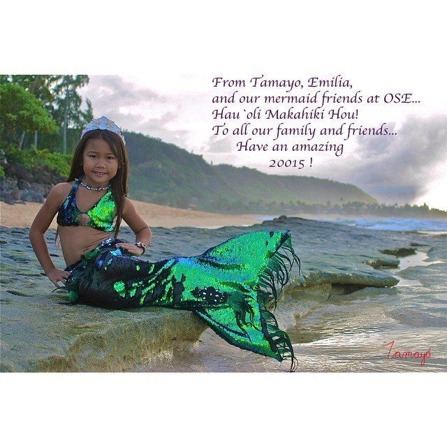A little girl in a mermaid costume is sitting on a rock on the beach