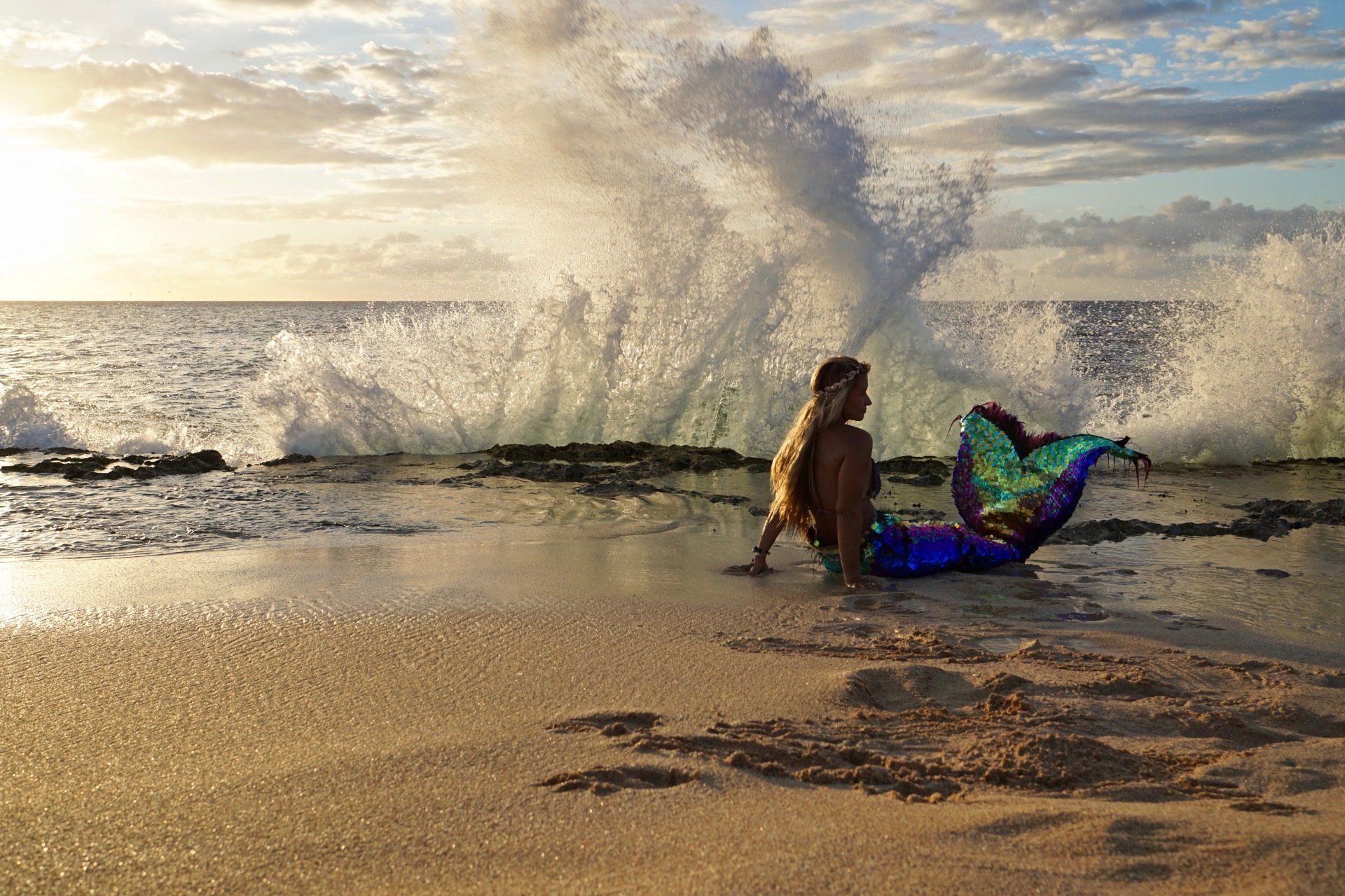 A mermaid is sitting on the beach looking at the ocean waves.