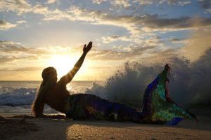 A mermaid is laying on the beach at sunset.