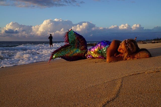 A woman in a mermaid costume is laying on the beach.