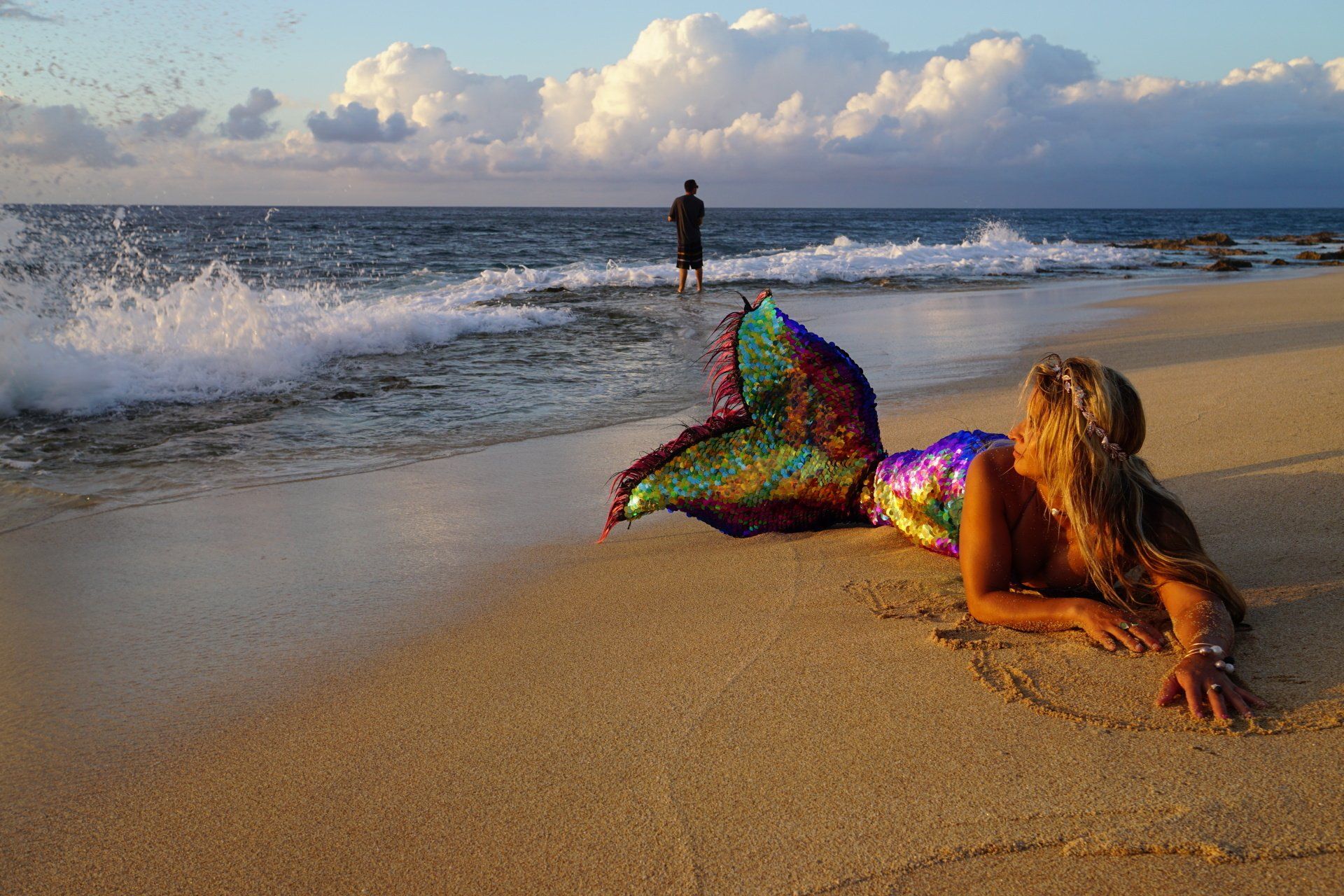 A woman in a mermaid costume is laying on the beach.
